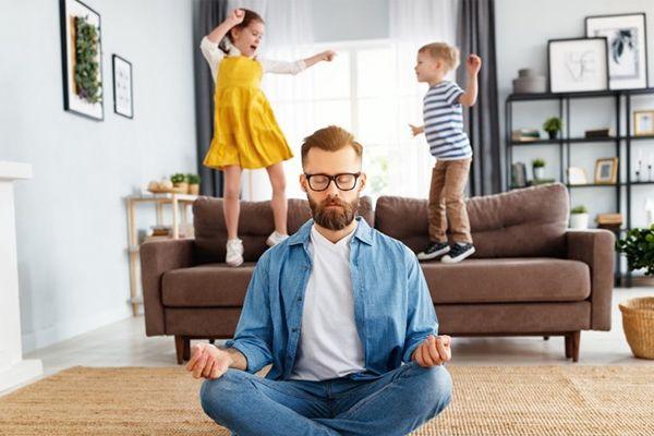man meditating while children jump on the sofa