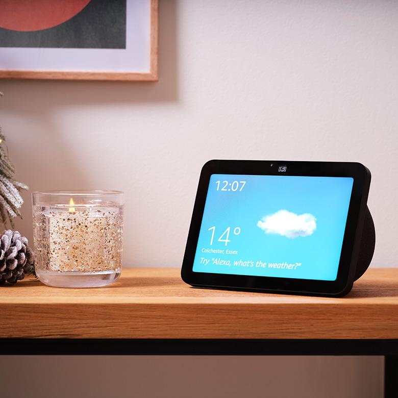 an amazon echo show 8 next to a candle on a table