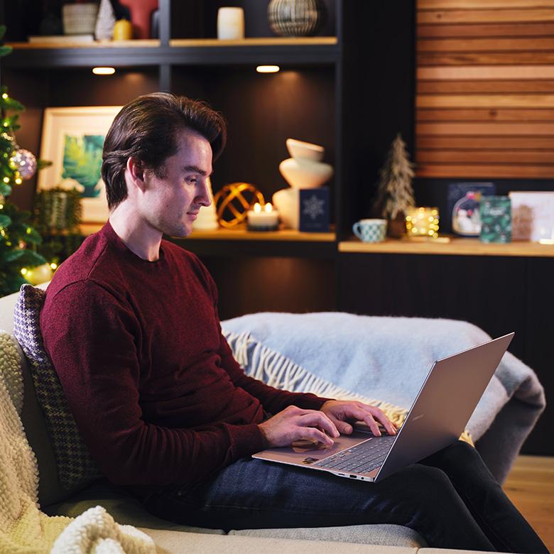 a man sitting on a couch with a samsung galaxy book 4 edge laptop on his lap