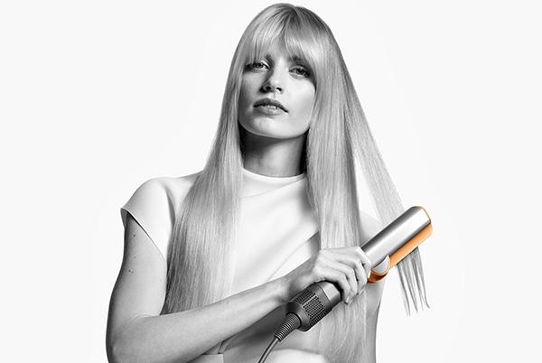 a woman with long blonde hair using a dyson airstrait straightener