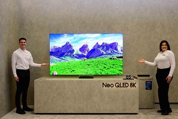 two people standing next to a samsung neo qled 8k qn990f tv at ces 2025