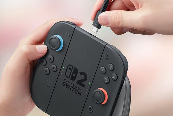 a person holding a nintendo switch 2 charging grip and plugging a cable into the top of it