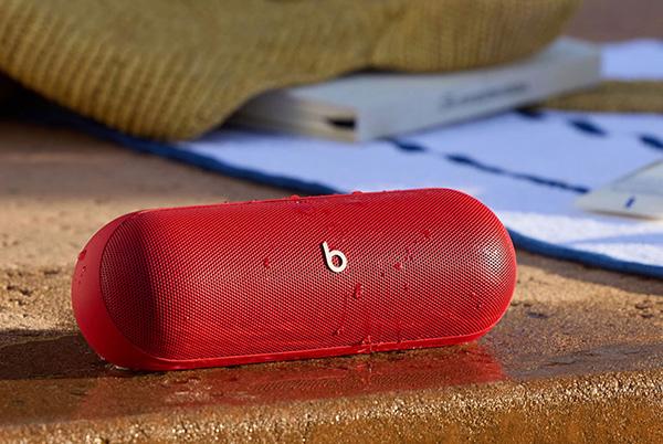 a red beats pill portable speaker sitting on a concrete surface next to a laptop
