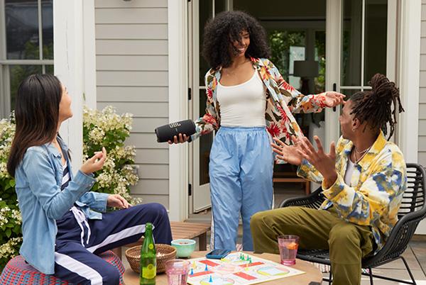 three people sitting on a patio talking with woman holding a jbl charge 5 wi-fi speaker