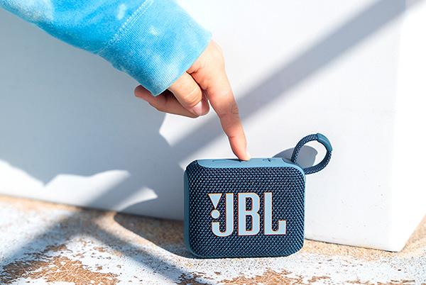a person pointing to a jbl go 4 bluetooth portable speaker on the ground