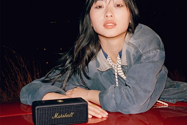 a woman laying on a red car with a marshall emberton ii portable speaker