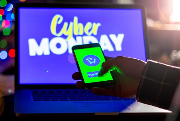 Cyber Monday on laptop screen with phone in hand