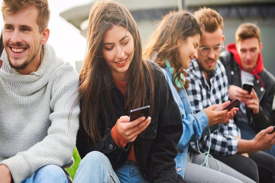 A woman sitting with other people looking at a smart phone and smiling