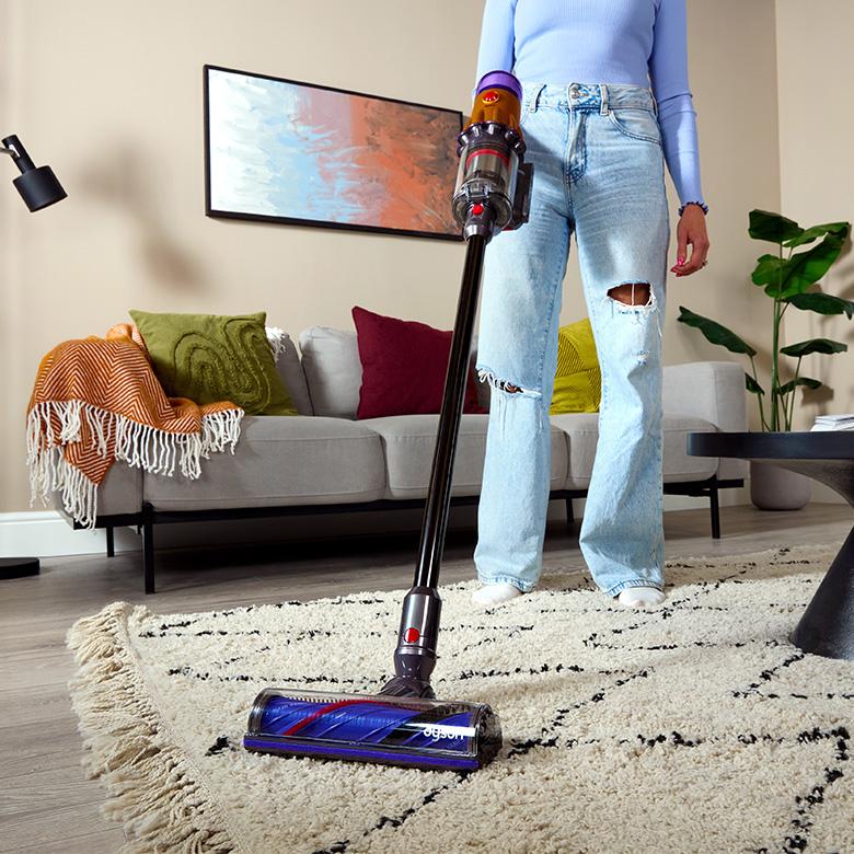 a woman standing in a living room with a dyson vacuum