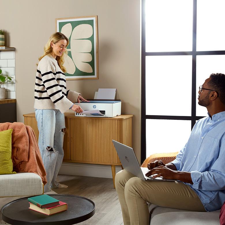 a man and woman sitting in a living room with a laptop and printer