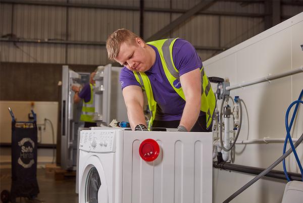 a man in a yellow vest is working on a washing machine