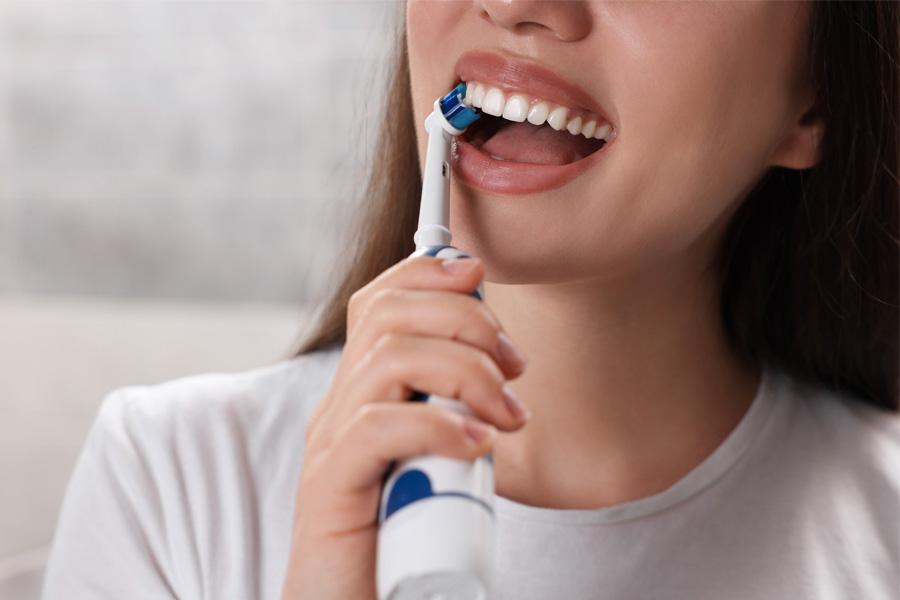 a woman brushing her teeth with an electric toothbrush