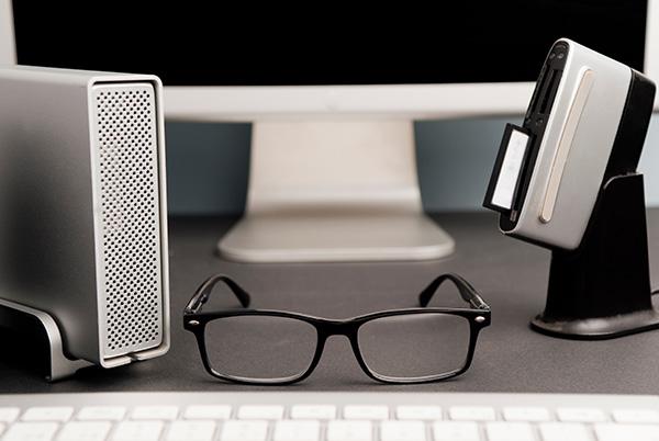 a hard drive, pair of glasses, and keyboard on a desk in front of a computer monitor