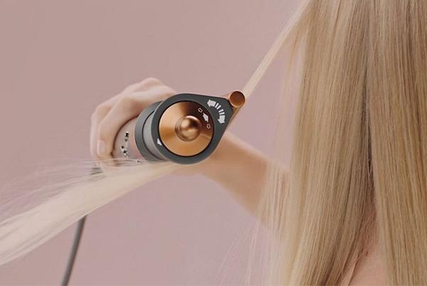 a woman blow drying her long blonde hair with a dyson airwrap coanda smoothing dryer
