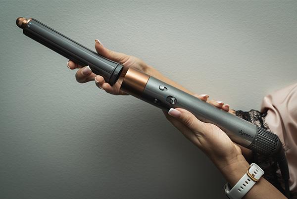 a woman holding a dyson airwrap multi styler putting the curling barrel attachment on
