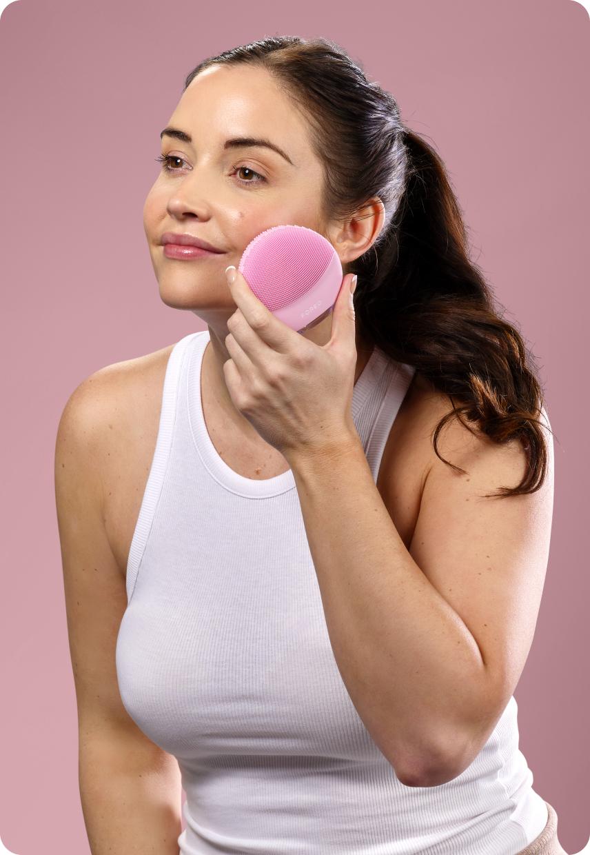 A woman using a cleanser brush on her face