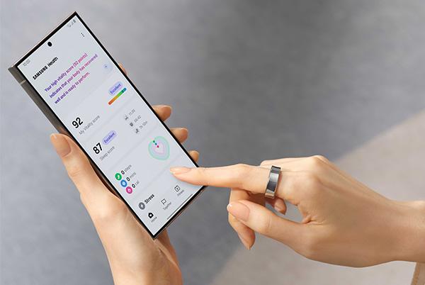 a woman holding a smart phone with a finger wearing a smart ring pressing the screen