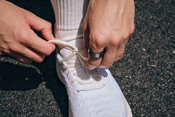 a person tying a white running shoe while wearing a smart ring