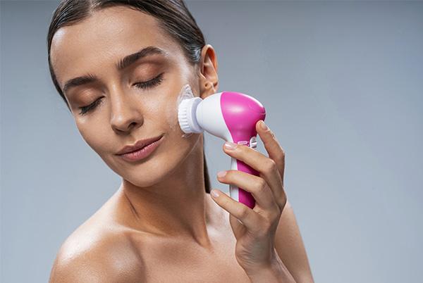 a woman using a pink and white facial cleansing brush on her face