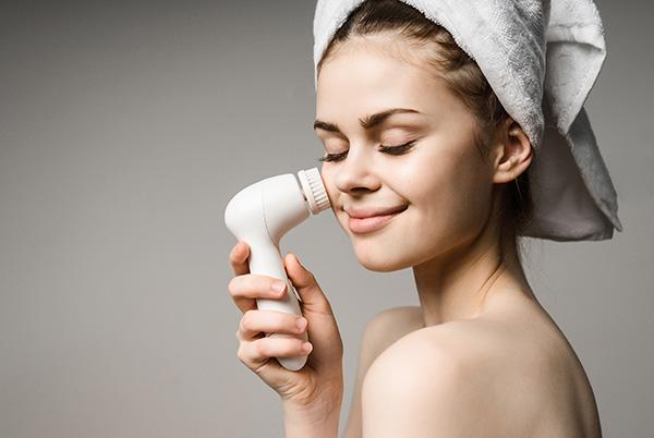 a woman with a towel on her head using a face cleansing brush