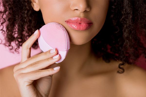 a woman with curly hair holding a silicone face cleansing brush against her cheek