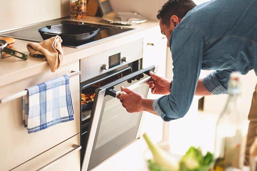 A person opening a modern built-in oven door in a kitchen