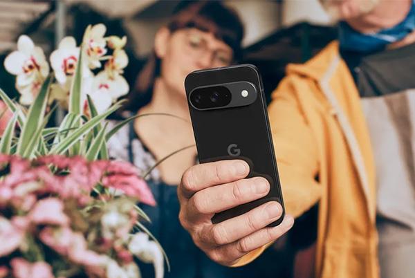 a man holding a google pixel 9 phone in front of a flower arrangement
