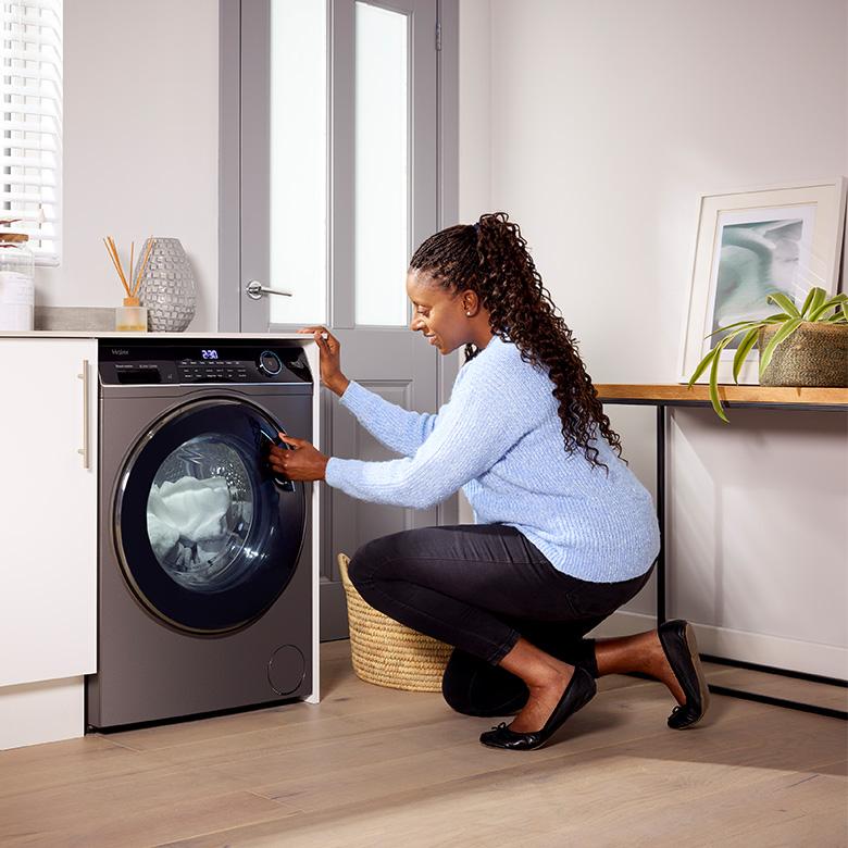 a woman is putting clothes into a haier i-pro series 5 washing machine