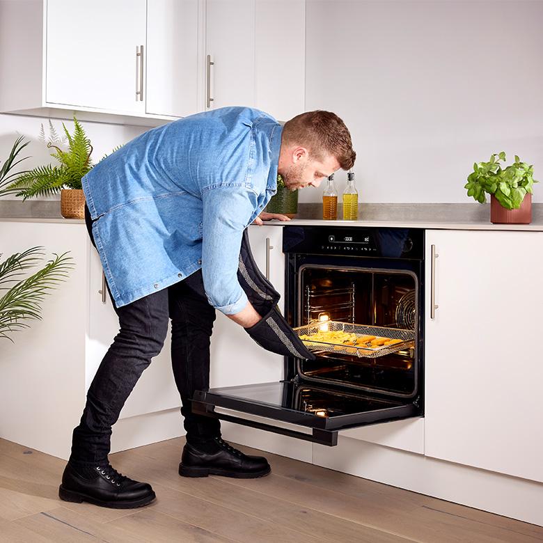a man in a blue jacket is taking food out of a hisense hi6 blackline airfry smart oven