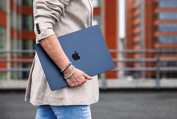 a woman holding a blue macbook in her hand while walking