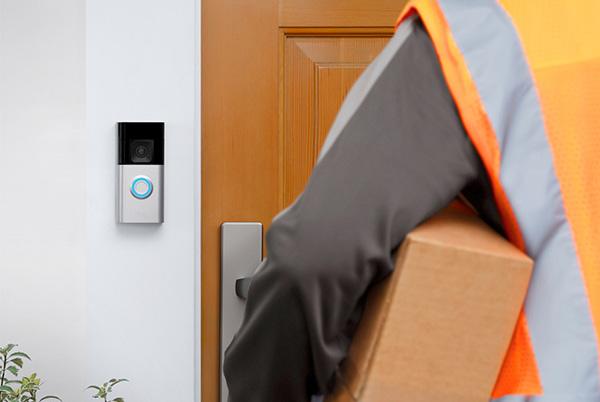 a man in orange vest holding a package and walking towards a door with a ring doorbell next to it