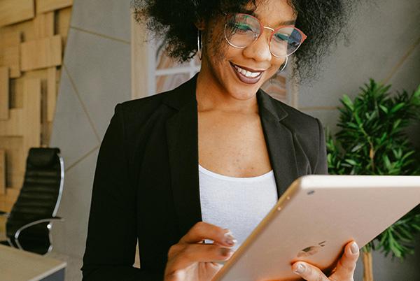 a woman with glasses and curly hair smiling while using ipad