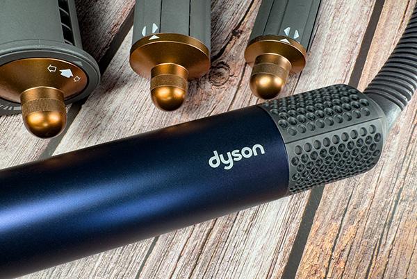 close up of a blue dyson airwrap handle and filter with various attachments in the background