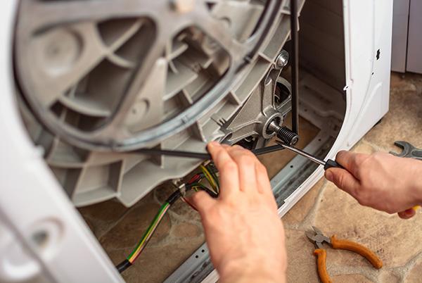 a person is working on a washing machine with a pair of pliers