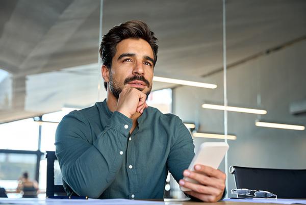 Man looking pensive holding phone at desk