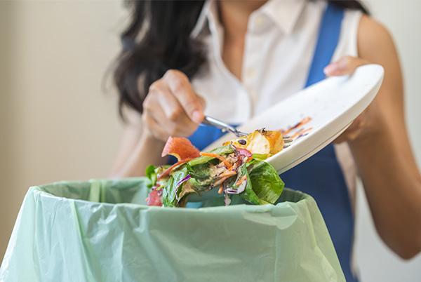 a woman in a blue apron scraping food off a plate into a bin