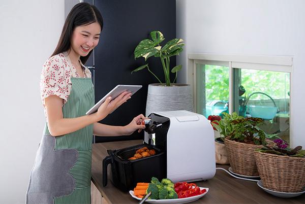 a woman in apron using a tablet to cook food in an air fryer