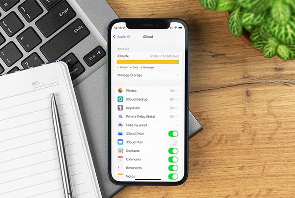 an iphone sitting on top of a wooden table next to a laptop with icloud storage info on screen