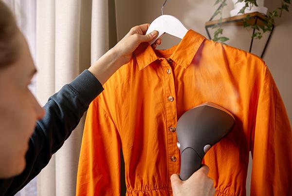 woman using clothes steamer on orange shirt