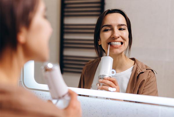 a woman using a water flosser in front of a mirror