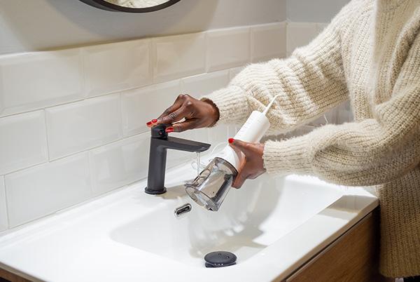 a woman filling a water flosser reservoir under a bathroom tap
