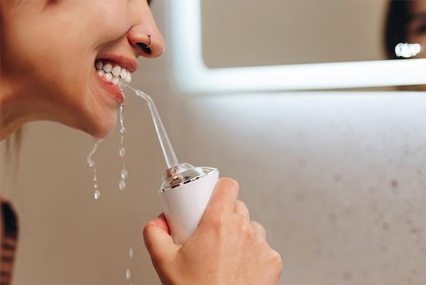 a woman rinsing her teeth with a water flosser