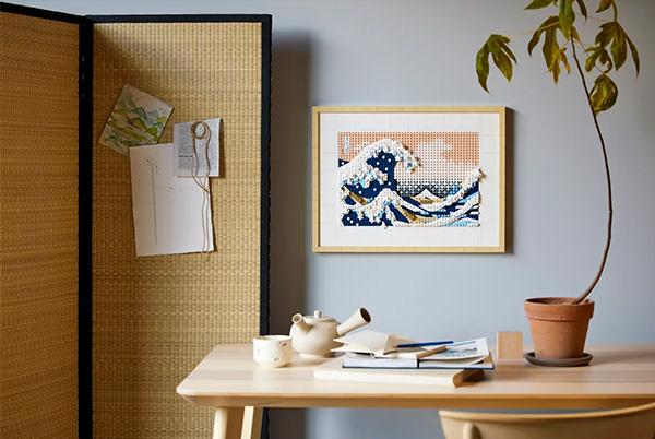 a room with a table and a plant on it with hokusai's the great wave lego set framed and hung on the wall
