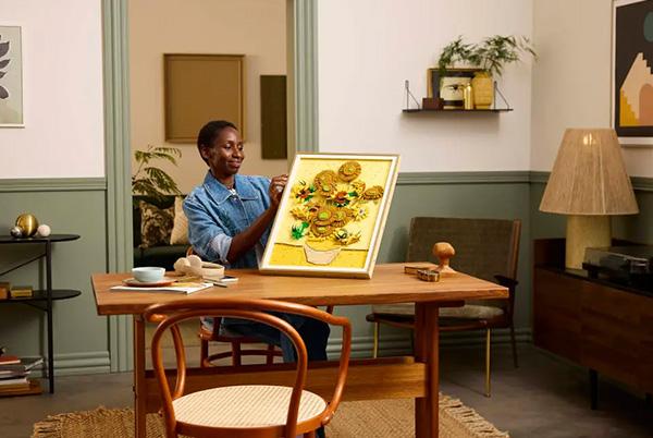 a woman sitting at a table holding up the lego art vincent van gogh sunflowers set in a frame