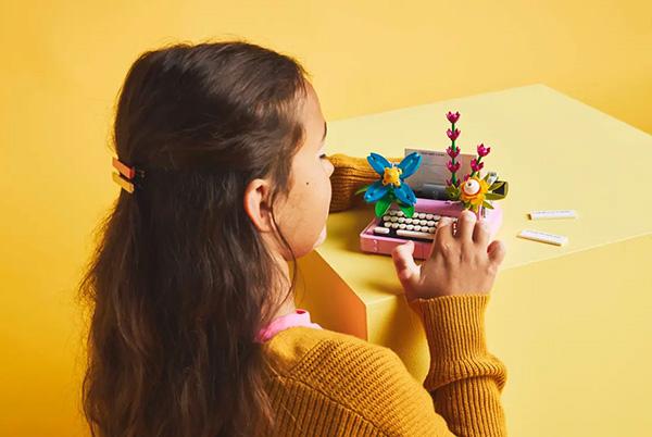 a young girl sitting on a yellow table with a lego creator typewriter with flowers