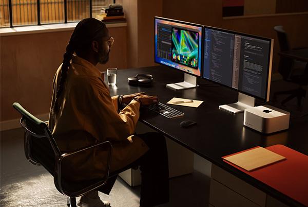 a man sitting at a desk with two monitors and a keyboard using mac studio