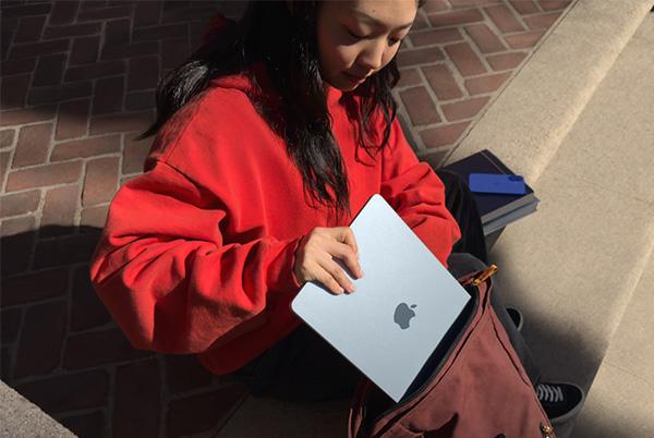 a woman sitting on the steps putting a macbook air into a bag