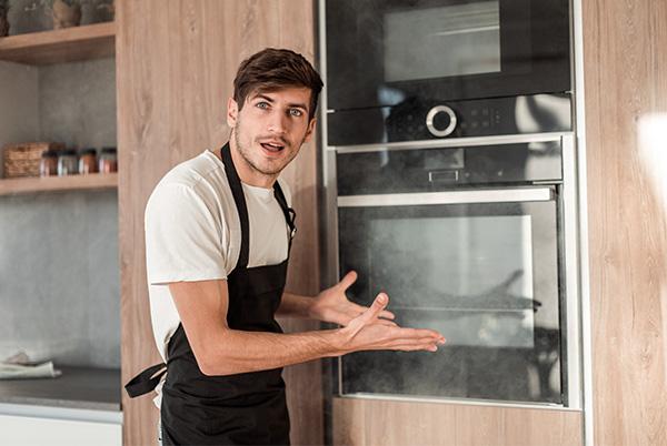 a man in a black apron standing in front of an oven