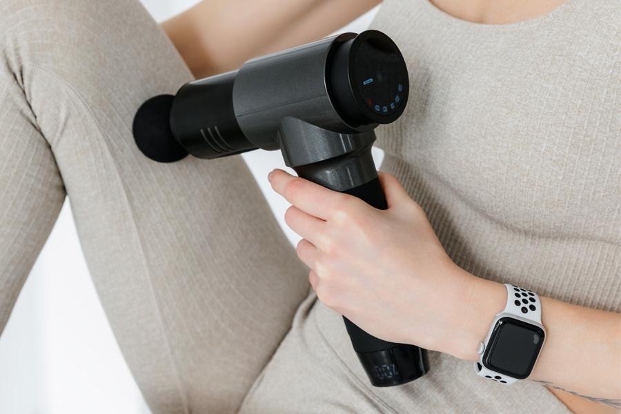 a woman in a white shirt massages her arm with a massage device
