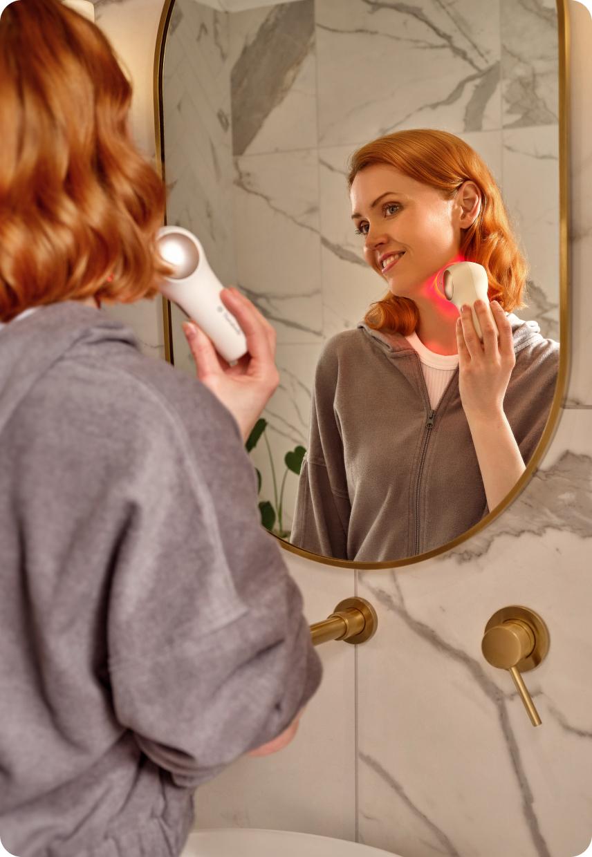 A lady looking in a mirror using a face massager